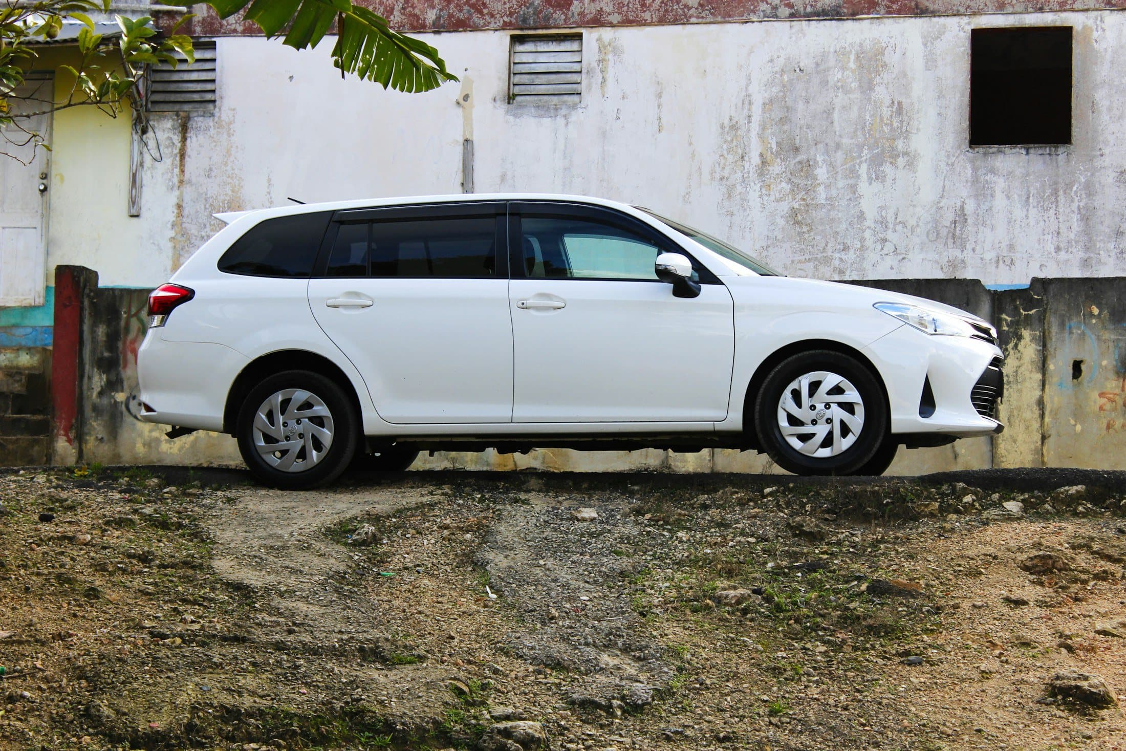 Eski bir duvarın önünde, toprak zeminde duran beyaz station wagon, yandan
