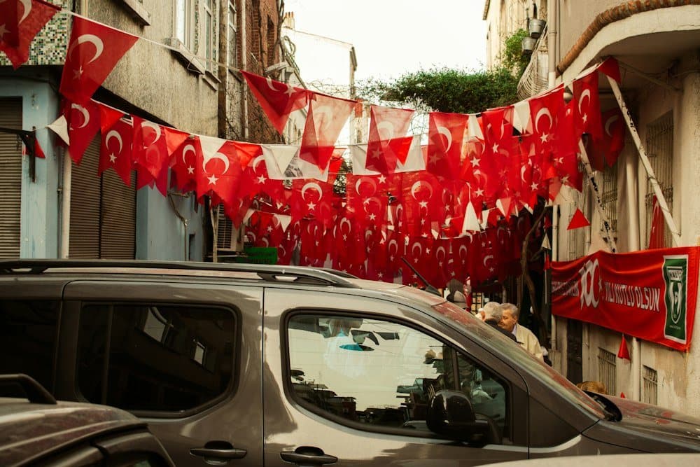 Türk bayraklarıyla süslü dar bir sokakta gri hafif ticari araç